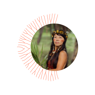 Mulher indígena jovem, cabelos longos caindo sobre o tronco, usa brinco e adorno de penas na cabeça. Rosto pintado olha séria para a frente. 